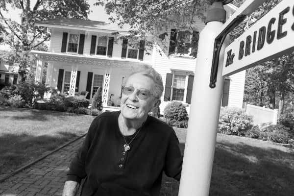 White woman standing in front yard next to sign reading "Bridges"