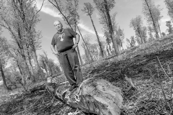 White man standing on a log with hands on hips.