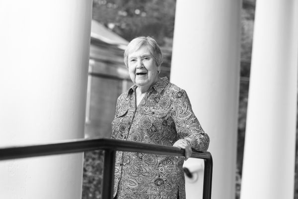 White woman standing between columns, holding railing.
